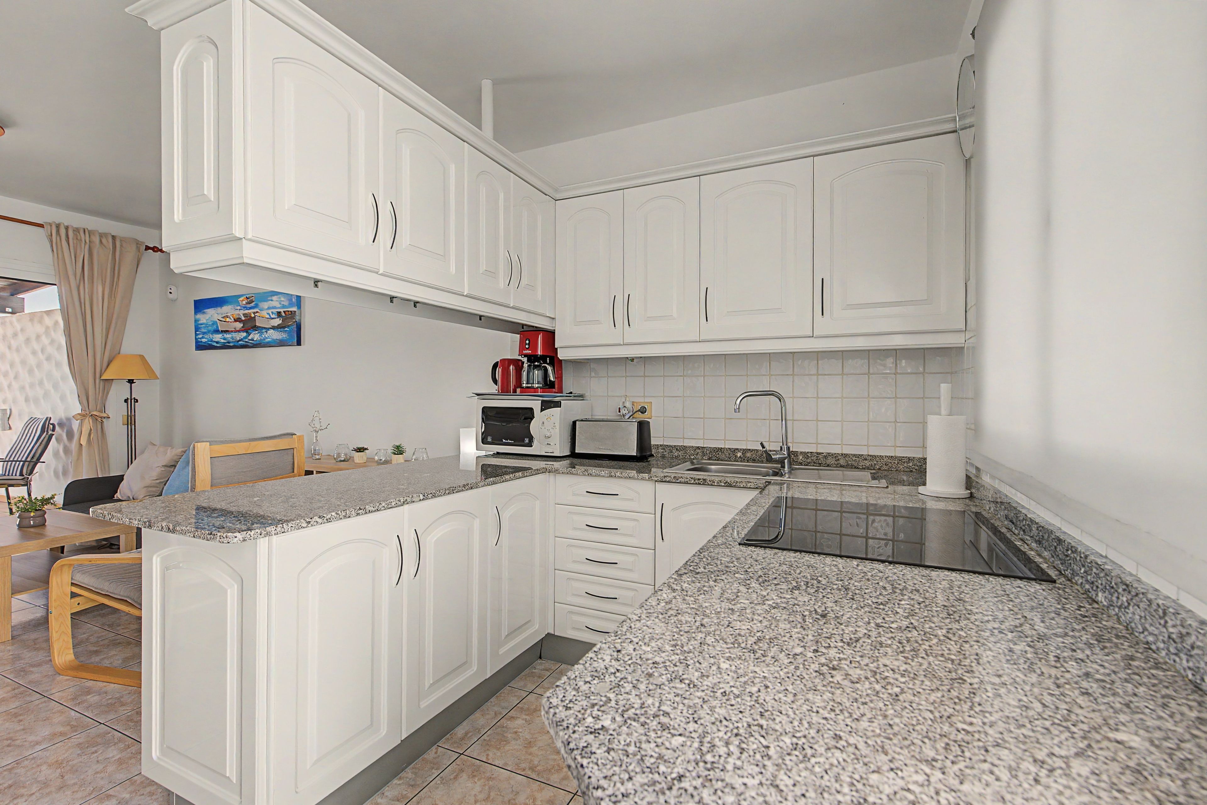 A kitchen with white cabinets, a red coffee maker, a toaster, and a sink.