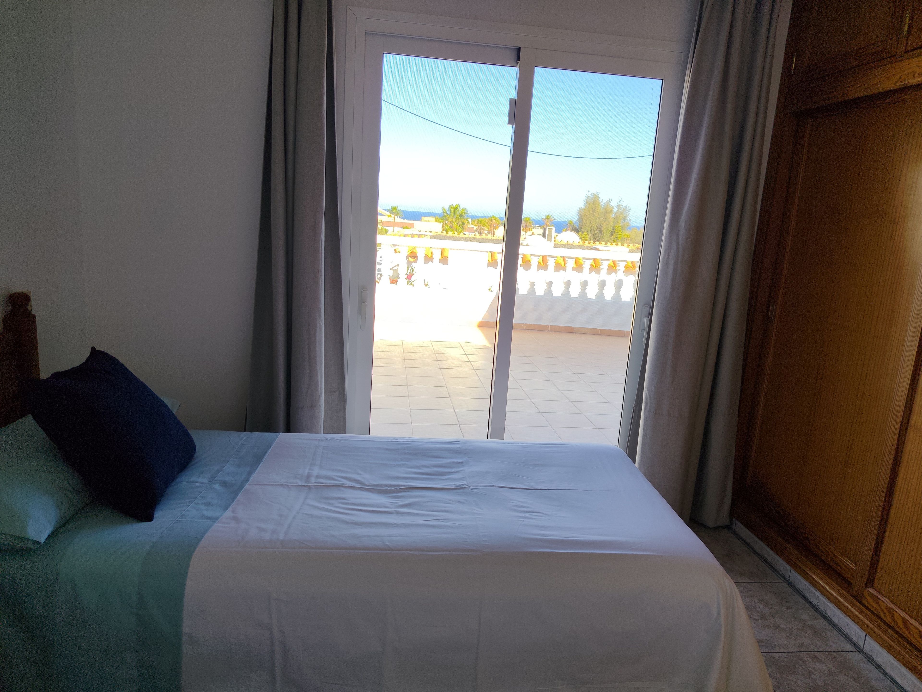Une chambre à coucher avec un lit, des rideaux et une vue sur un balcon doté d’une balustrade.
