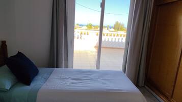 Une chambre à coucher avec un lit, des rideaux et une vue sur un balcon doté d’une balustrade.