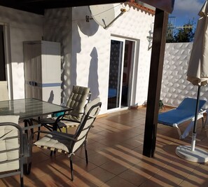 A patio with a table and chairs, a blue lounge chair, and a white wall with a textured pattern.