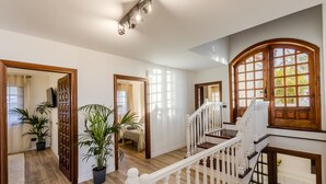 A spacious interior with a wooden staircase, potted plants, and large windows allowing natural light.