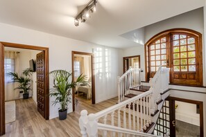 Un interior espacioso con una escalera de madera, plantas en macetas y ventanas amplias que dejan entrar luz natural.