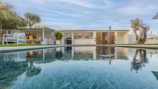 A swimming pool with a patio area, a kitchen, and a dining area.