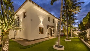 A white building with a tiled roof, surrounded by palm trees and a well-maintained lawn.