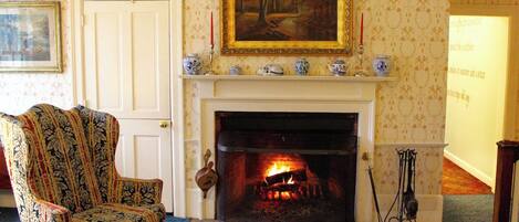 A room with a fireplace, a patterned armchair, and a painting on the wall.