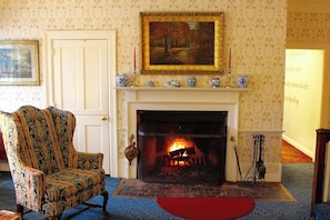 A room with a fireplace, a patterned armchair, and a painting on the wall.