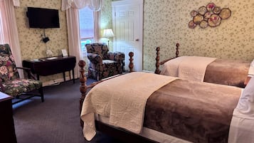 A hotel room with two beds, a desk, a chair, a TV, and a door.