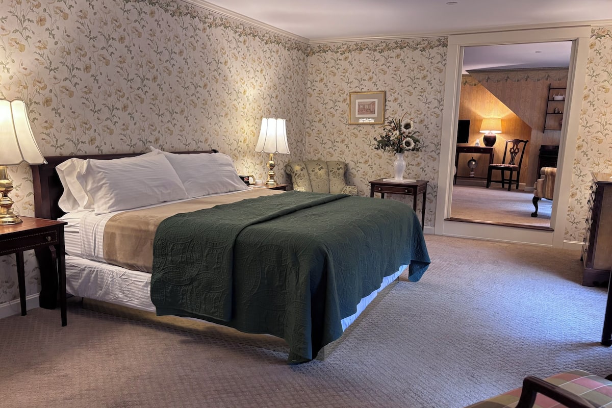 A neatly arranged bedroom with a bed, two bedside tables, a lamp, a vase with flowers, and a framed picture on the wall.