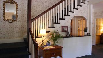 A staircase with a wooden handrail and white balusters, leading to a landing with a desk, a vase with flowers, and a framed picture.