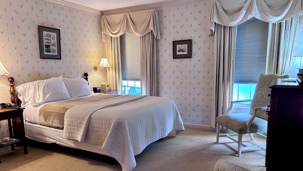 A neatly arranged hotel room with a bed, a chair, a desk, and two framed pictures on the wall. - Deerfield Inn (Deerfield)