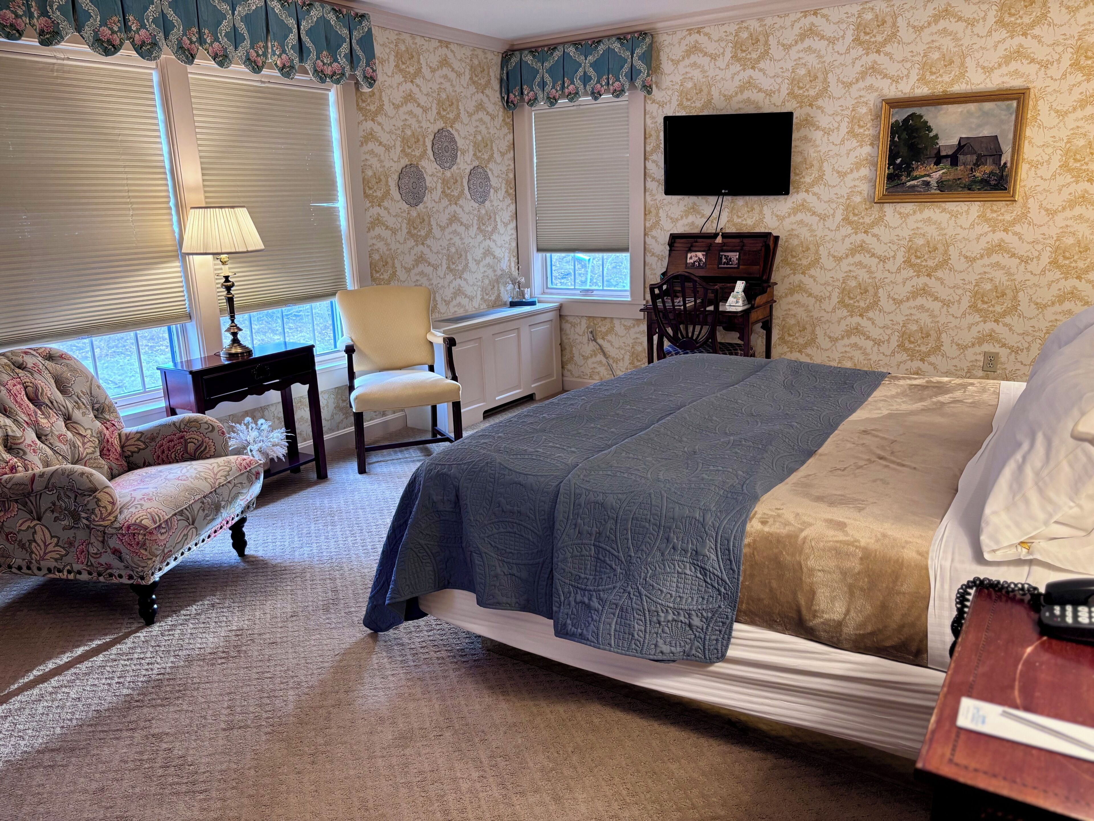 A bedroom with a bed, a chair, a desk, a lamp, and a television.