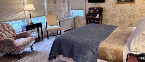 A bedroom with a bed, a chair, a desk, a lamp, and a television.