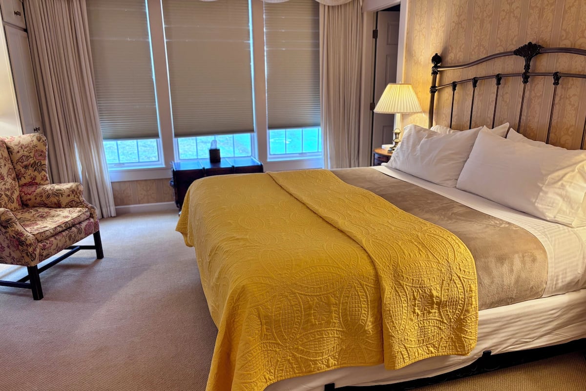 A hotel room with a bed, a chair, a lamp, and a window with curtains.