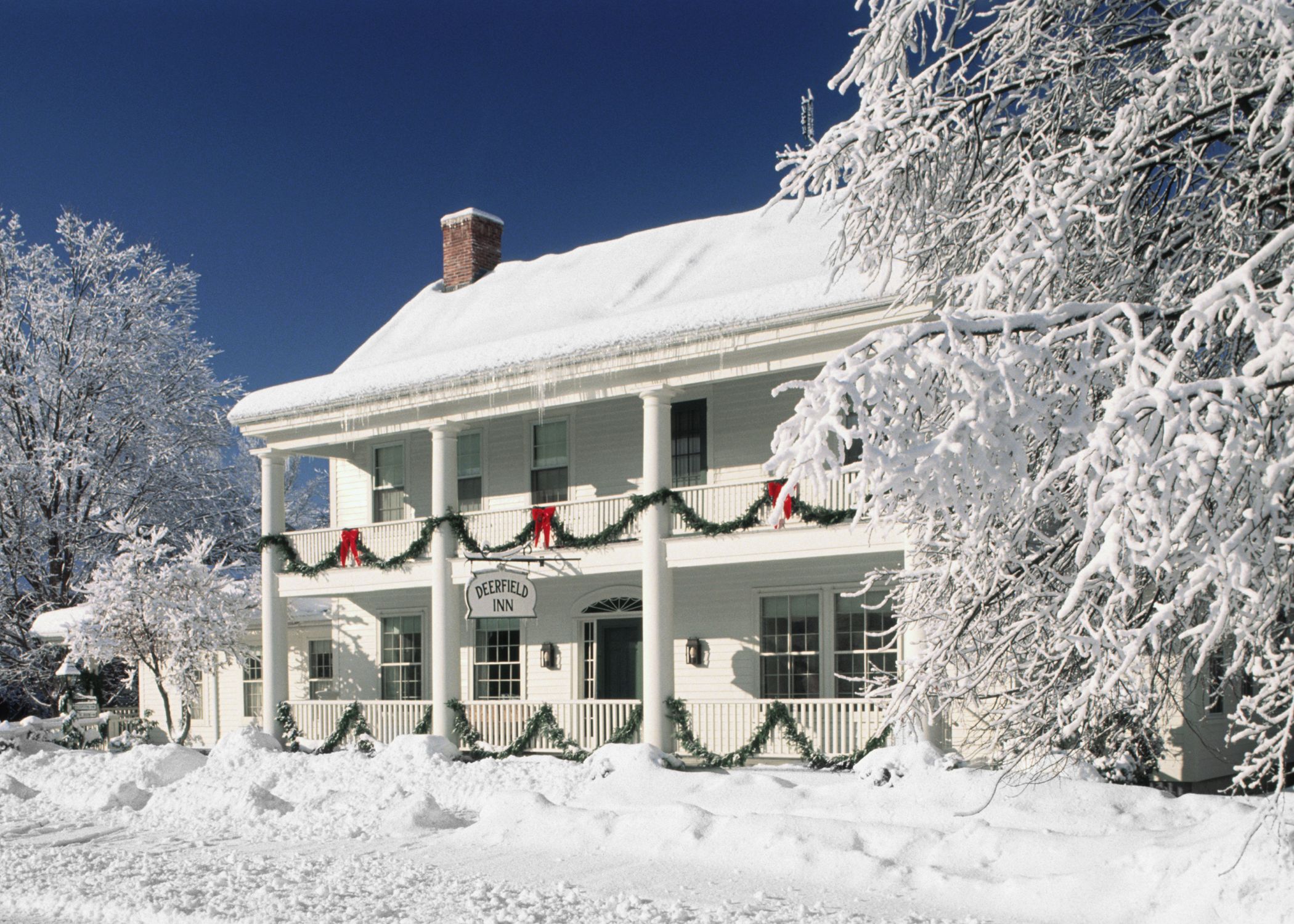 A snow-covered building with a porch, columns, and a sign that reads 'Deerfield Inn.'
