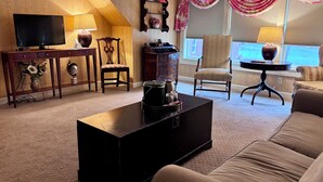 A living room with a TV, a coffee table, a sofa, a chair, and a lamp. - Deerfield Inn (Deerfield)
