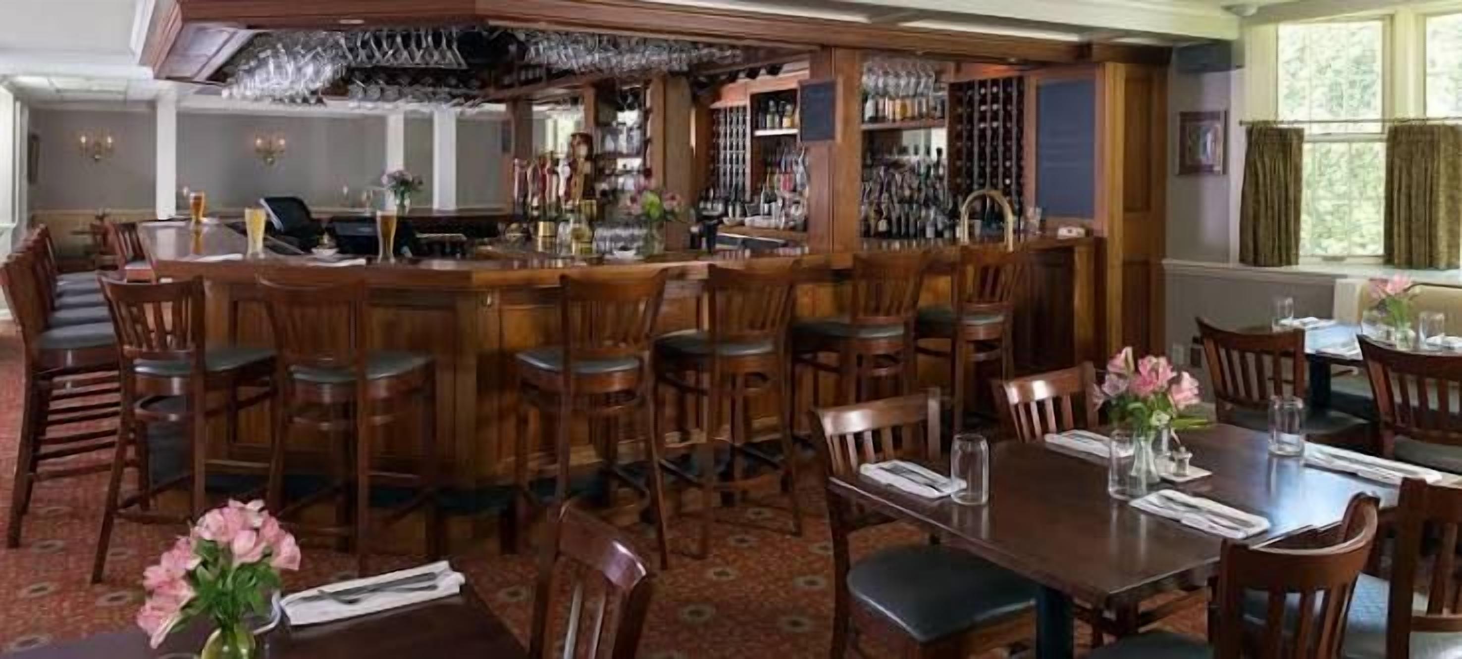 A bar area with wooden bar stools and a counter, surrounded by dining tables and chairs.
