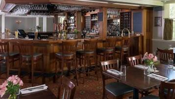 A bar area with wooden bar stools and a counter, surrounded by dining tables and chairs.