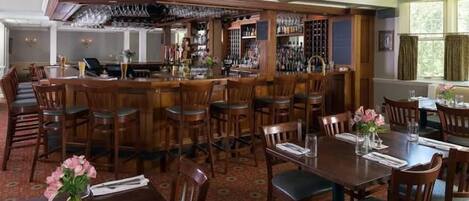 Zona de bar con taburetes de madera y una barra, rodeada de mesas y sillas para comer.