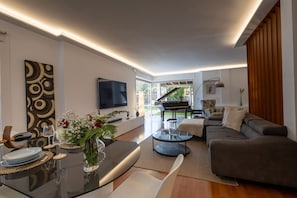 A modern living room with a sofa, coffee table, TV, and a dining area with plates and glasses.