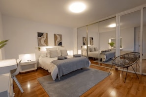 A modern bedroom with a bed, bedside tables, a chair, a mirror, and a large window.
