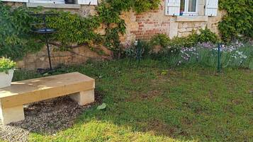 Un jardin avec un banc, un pot de fleurs et un mur de briques recouvert de lierre.