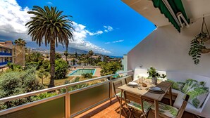 Ein Balkon mit Tisch und Stühlen, mit Blick auf einen Pool und Grünflächen.