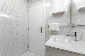 Een moderne badkamer met witte marmeren tegels, een wit wastafelmeubel met chromen kraan en een douchecabine van glas.