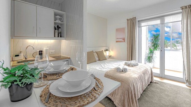 A modern hotel room with a kitchen area, a bed with a view, and a dining setup. - Studio with city view N8 (Puerto de la Cruz)