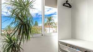 A room with a large window, a potted plant, white shelving, and a hanging black hanger. - Studio with city view N8 (Puerto de la Cruz)