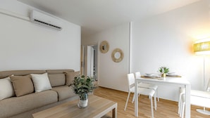 A modern living room with a sofa, a coffee table with a plant, a dining area with a table and chairs, and an air conditioning unit on the wall. - Sea and viewpoint view N3 (Puerto de la Cruz)