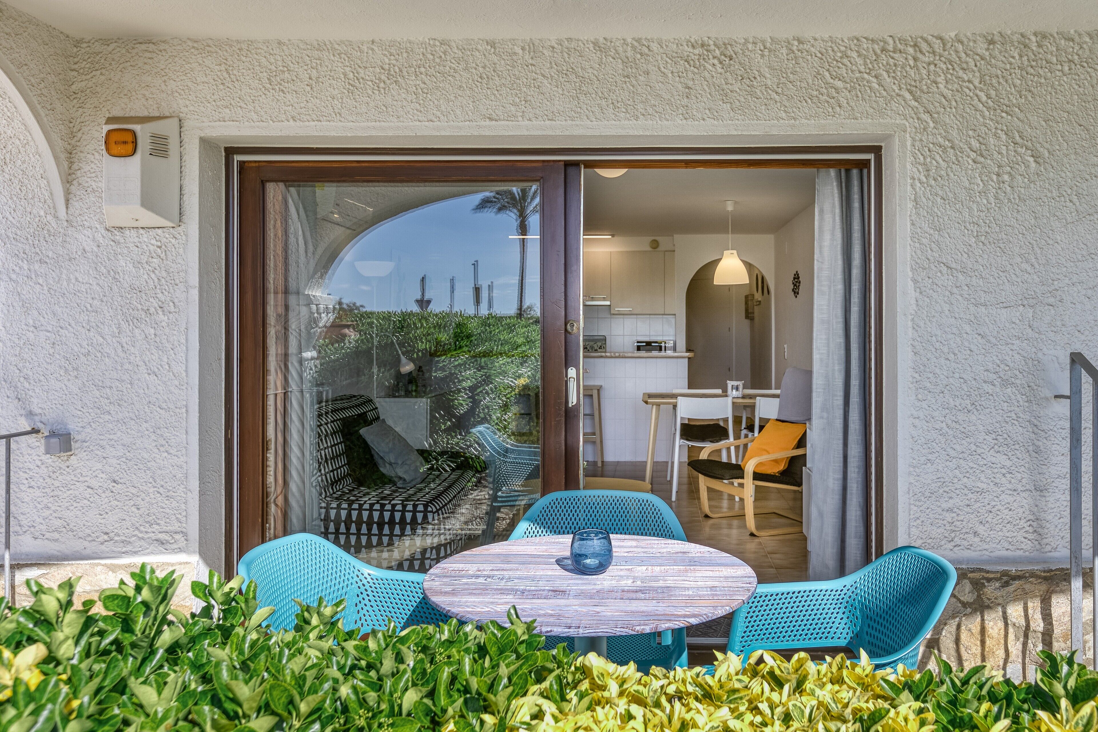 A patio with a table and chairs, a sliding glass door leading to a kitchen, and a white textured wall.