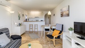 En moderne stue med sofa, sofabord, fjernsyn og et køkken i baggrunden.
