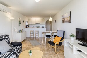 Ein modernes Wohnzimmer mit Sofa, Couchtisch, Fernseher und einer Küche im Hintergrund.