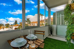 A dining area with a table set for two, large windows, and a view of buildings and palm trees. - Sea and viewpoint view N6 (Puerto de la Cruz)