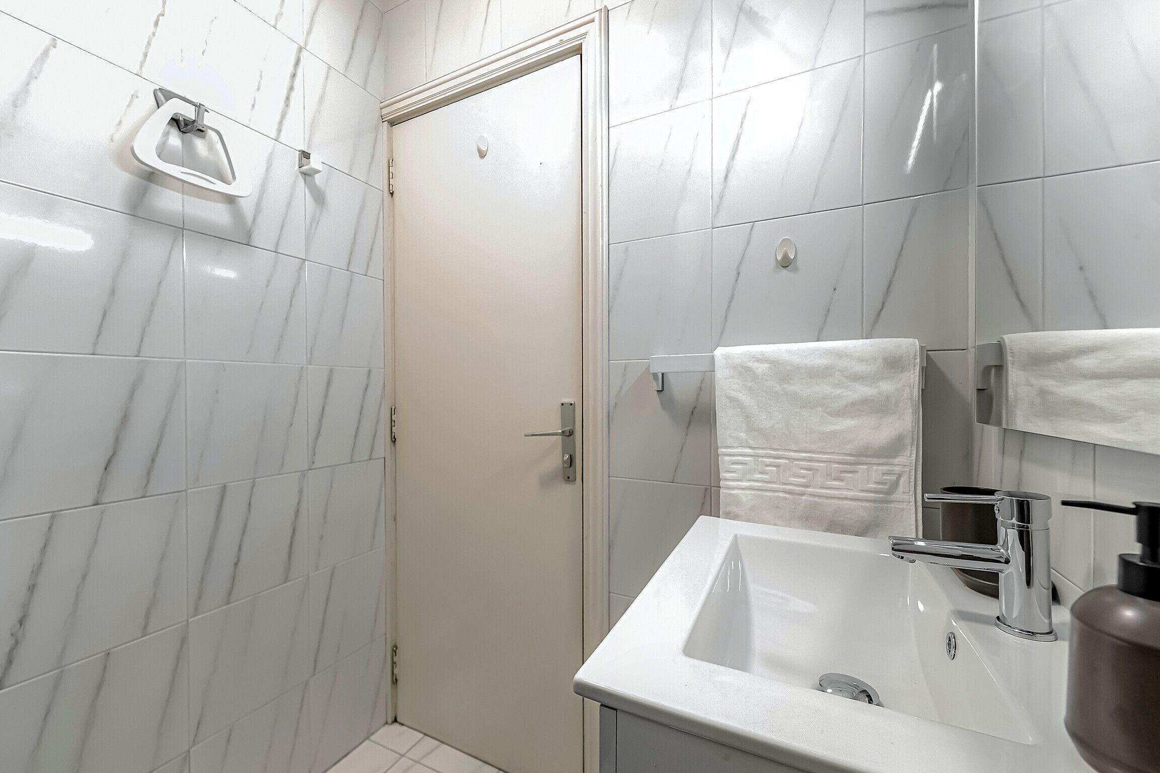 A bathroom with white marble tiles, a white sink, a mirror, and a towel rack.
