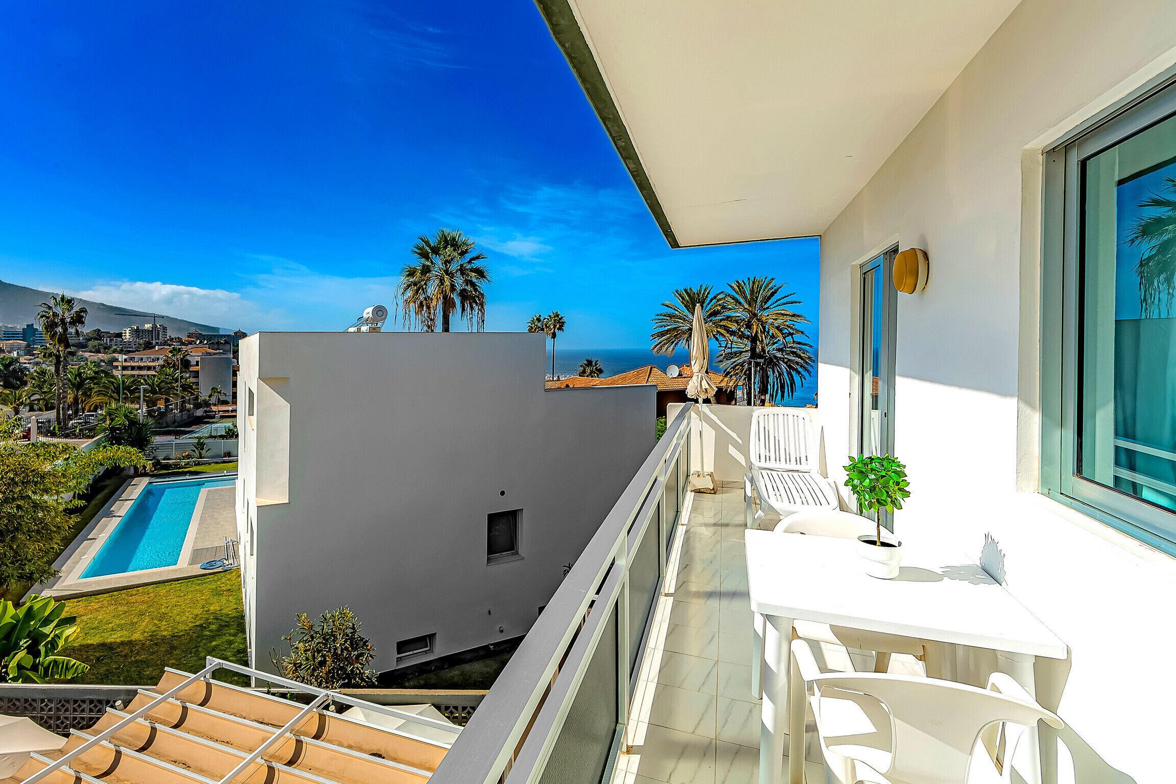A balcony with a pool, palm trees, and a view of the city.