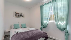 Een slaapkamer met een bed, een raam met gordijnen, een kunstwerk aan de muur en een plafondlamp.