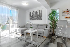 Ein modernes Wohnzimmer mit einem grauen Sofa, einem weißen Couchtisch, einer großen Kühlpflanze und einem gerahmten Bild an der Wand.