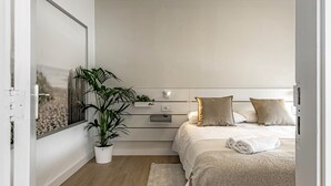 Une chambre à coucher moderne avec un lit, des tables de chevet, une plante en pot et une vue par la fenêtre.