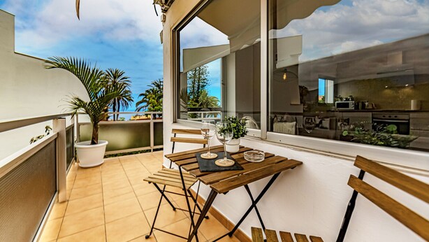 Un balcon avec une table en bois, des chaises et un pot de fleurs.