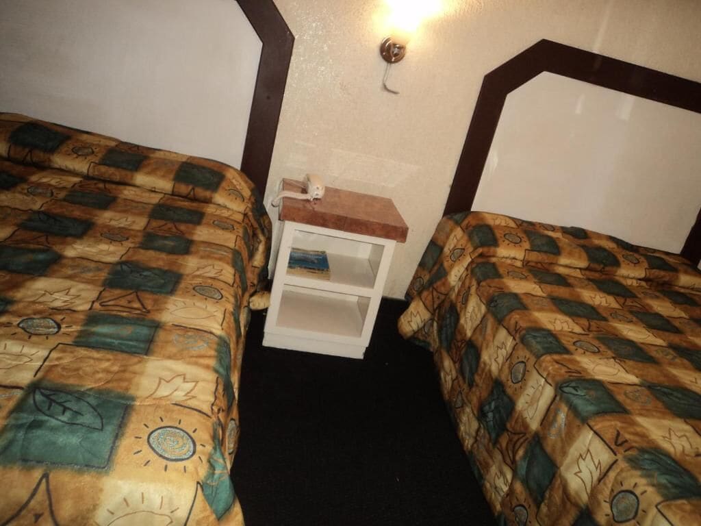Una habitación con dos camas, una mesita de noche y una lámpara en la pared.