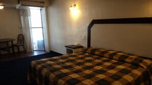 Une chambre d’hôtel avec un lit, une petite table, une chaise, une table de chevet et une fenêtre avec des rideaux.