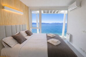 A bedroom with a bed, pillows, a bedside table with towels, a view of the sea, and an air conditioning unit. - Signature Lake View, Luxury Residences - Unit B06 (San Carlos de Bariloche)