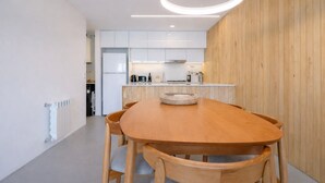 A modern kitchen with white cabinets, a wooden dining table, and a circular light fixture. - Signature Lake View, Luxury Residences - Unit B06 (San Carlos de Bariloche)
