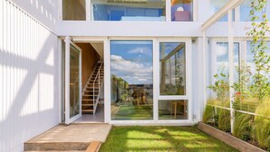 A modern two-story house with a visible staircase leading to the upper floor, a glass door entrance, and a small grassy yard. - Signature Lake View, Luxury Residences - Unit B06 (San Carlos de Bariloche)