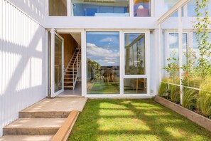A modern two-story house with a visible staircase leading to the upper floor, a glass door entrance, and a small grassy yard. - Signature Lake View, Luxury Residences - Unit B06 (San Carlos de Bariloche)