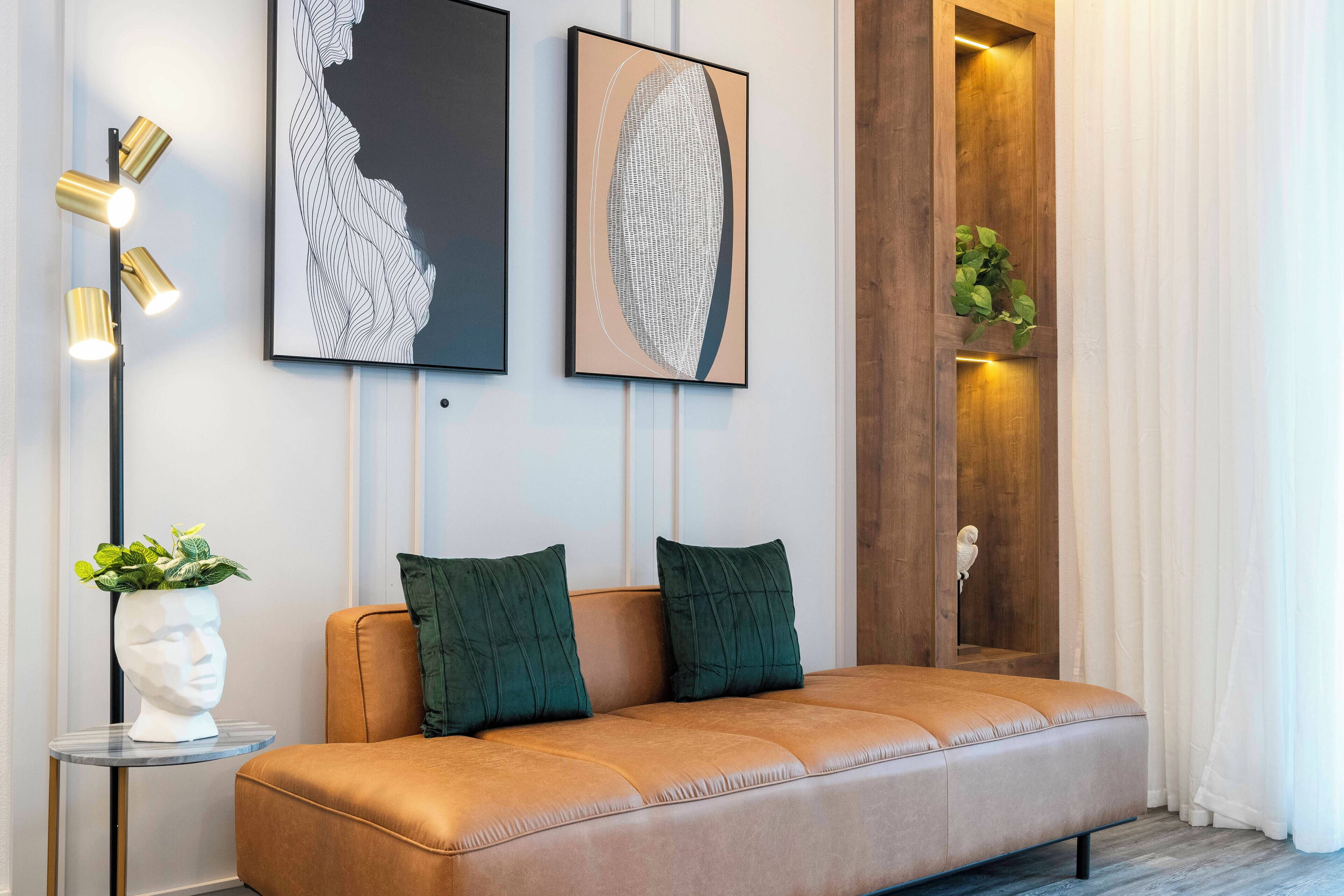 A modern living room with a leather sofa, two green cushions, a white bust sculpture, and two abstract art pieces on the wall.