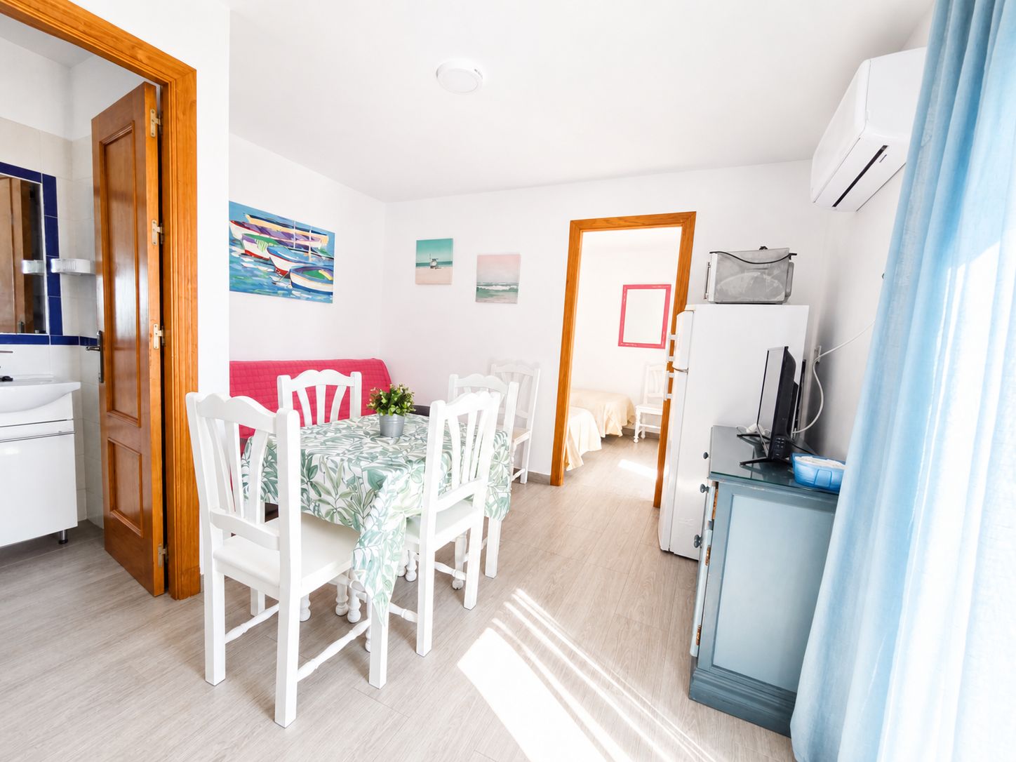 A bright room with a dining table, chairs, a sofa, and a kitchenette.