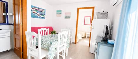 A bright room with a dining table, chairs, a sofa, and a kitchenette.