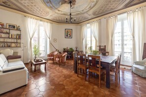 A spacious living room with a hexagonal tiled floor, a dining area with wooden furniture, and a ceiling with decorative plasterwork. - HAPPYFEW LA SUITE BARLA (Nice)